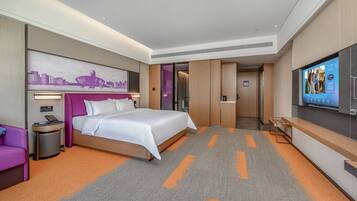 A modern hotel room with a large bed, a television, a desk, and a cityscape mural on the wall.