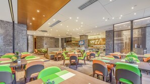 A modern dining area with multiple tables and chairs, a kitchen in the background, and a clean, well-lit environment. - Hampton by Hilton Dongguan Cntrl Square (Dongguan)