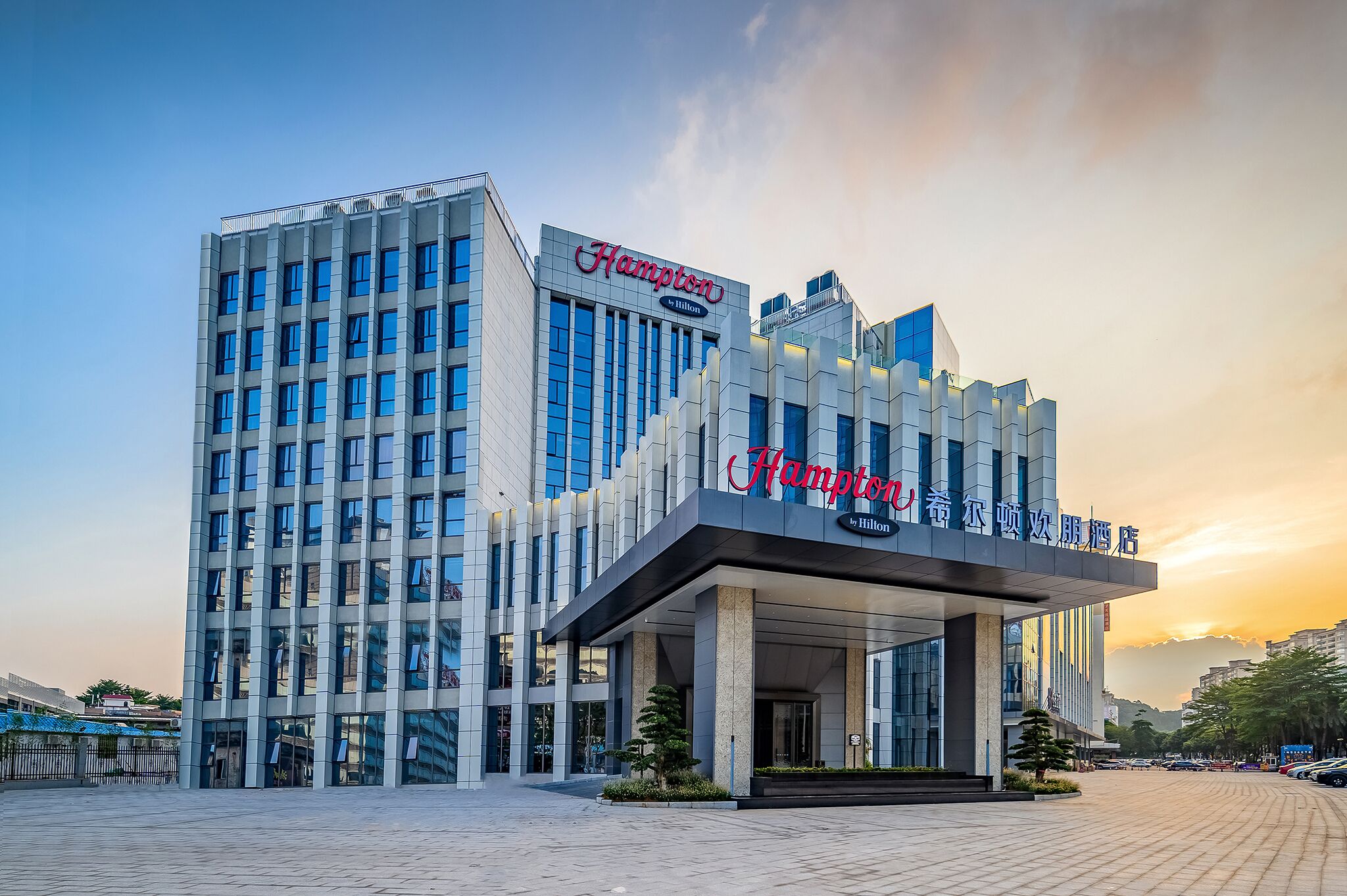A modern hotel with a prominent 'Hampton by Hilton' sign, featuring a sleek facade and a spacious entrance area.