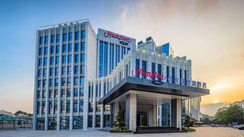 A modern hotel with a prominent 'Hampton by Hilton' sign, featuring a sleek facade and a spacious entrance area.