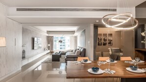 Un espace repas moderne avec une table en bois dressée pour quatre personnes, un canapé en arrière-plan et une vue sur la ville par la fenêtre.