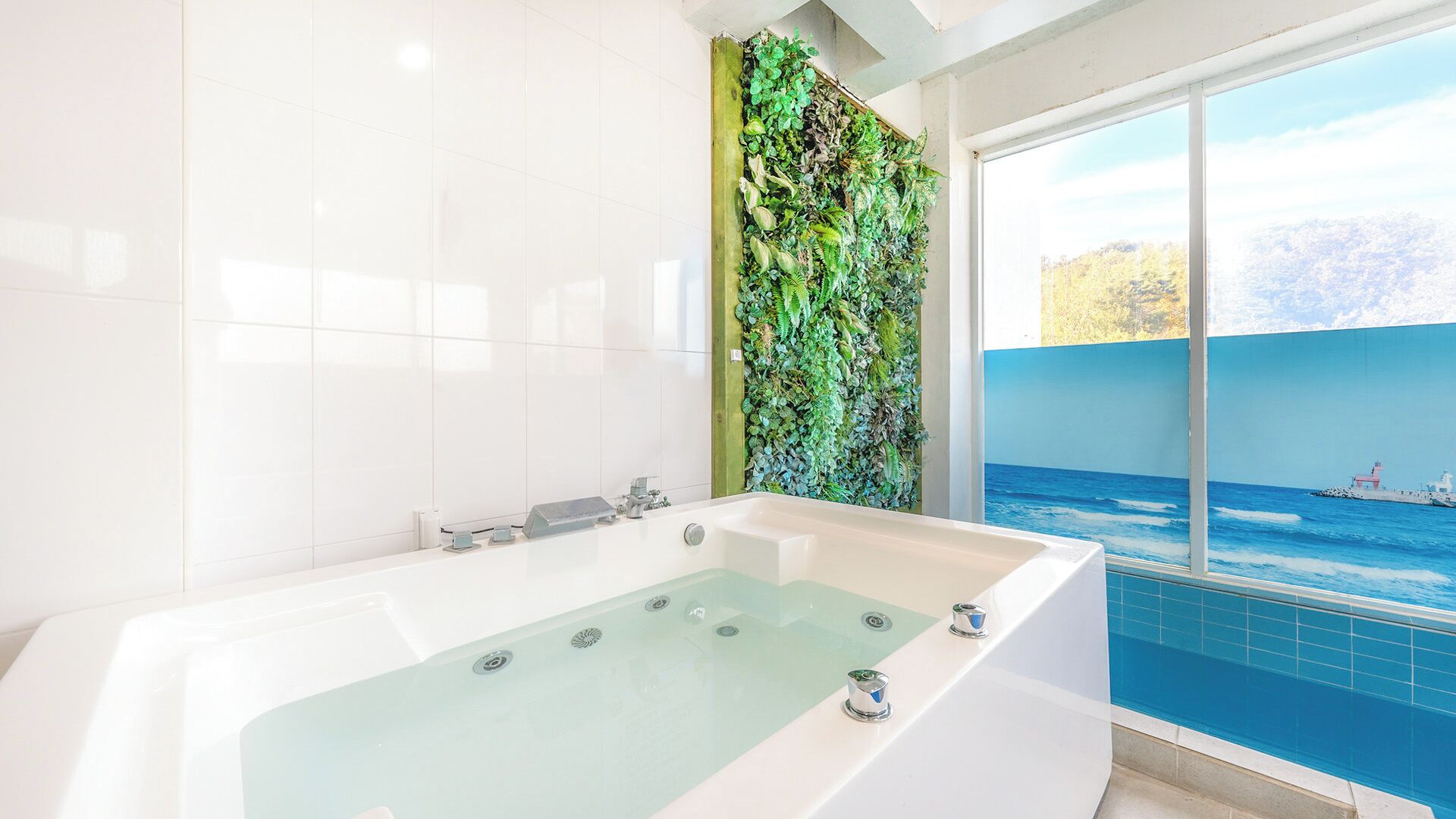 A modern bathroom with a large bathtub, a green vertical garden wall, and a view of the ocean through a large window.