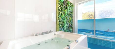 A modern bathroom with a large bathtub, a green vertical garden wall, and a view of the ocean through a large window.