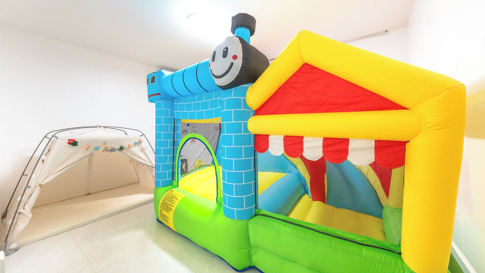 A colorful inflatable play structure with a blue and yellow design, a red and yellow house, and a small tent in the background.