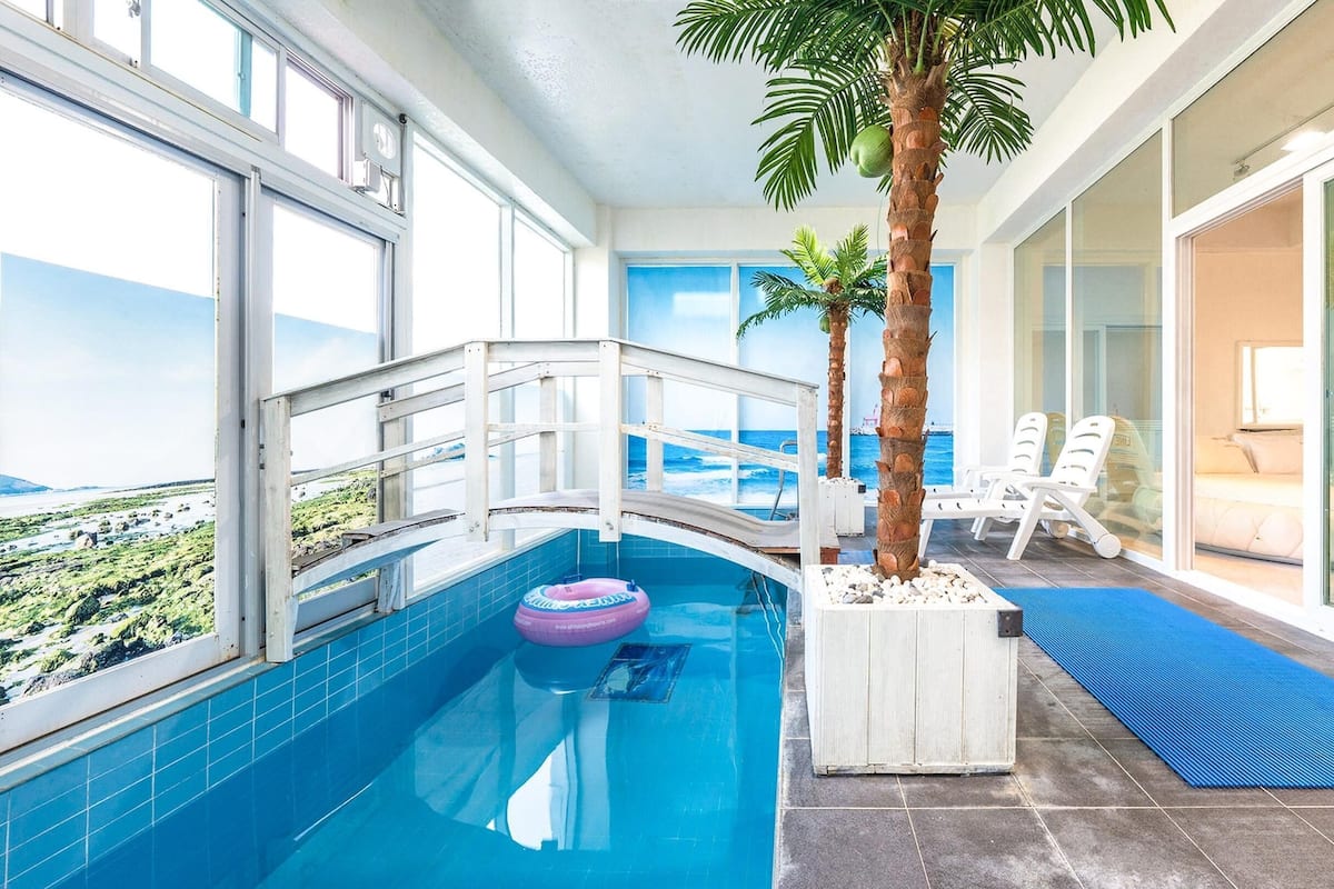 A pool area with a view of the ocean, a palm tree, and lounge chairs.
