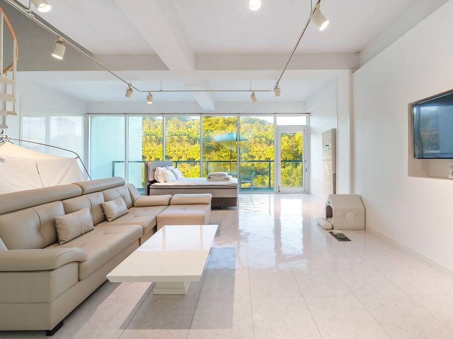 A modern living room with a sofa, a bed, a TV, and a staircase.