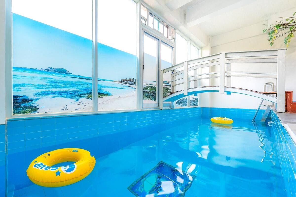 An indoor swimming pool with clear blue tiles, a yellow inflatable ring, and a mural of a beach scene.