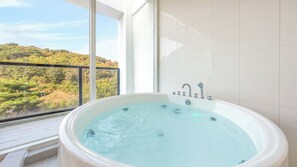 A bathroom with a large bathtub, a window with a view of a forest, and white tiled walls. - Gyeongju Lineview Poolvilla (Gyeongju)