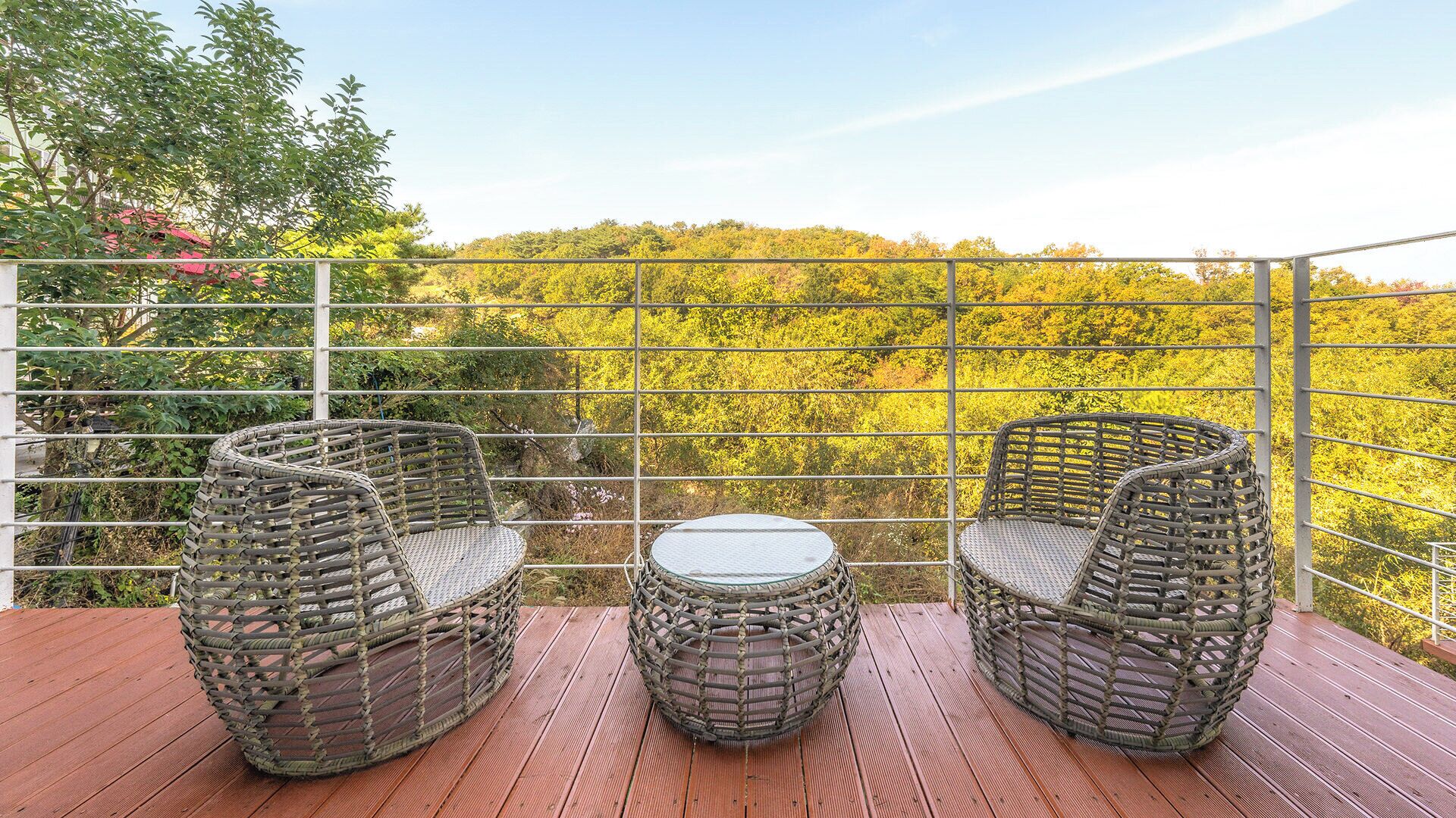 Une terrasse dotée de meubles en osier et d’une table, offrant une vue sur une zone boisée.