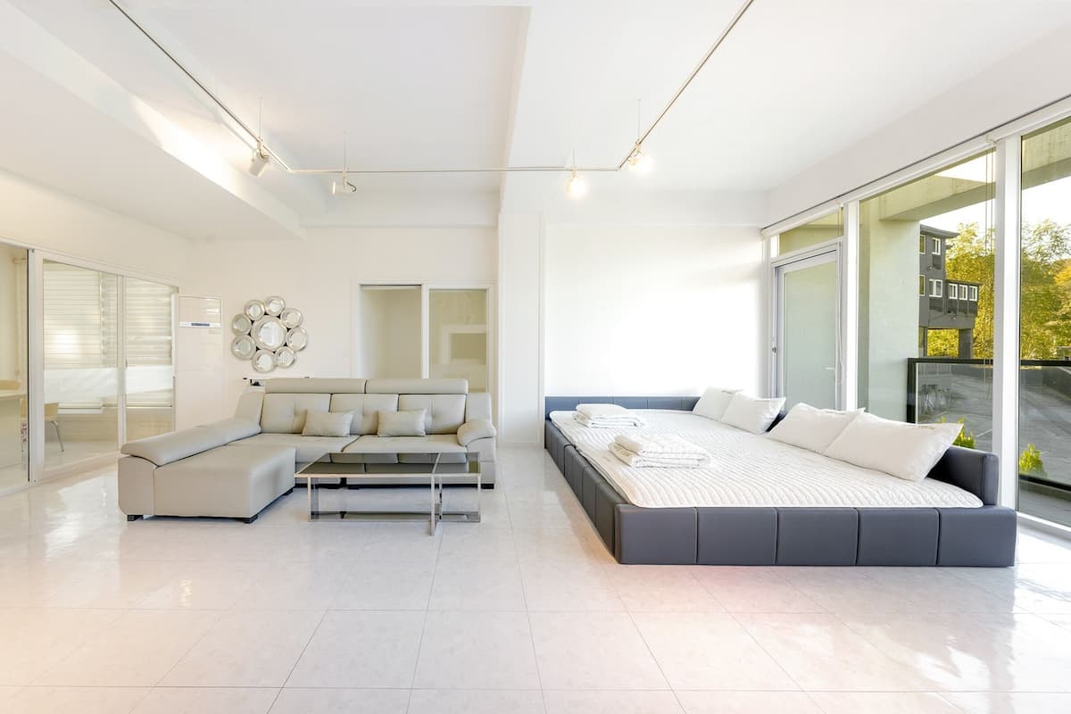A modern hotel room with a large bed, a sofa, a dining area, and a view of the city.