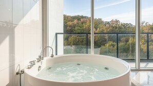 Un baño moderno con una bañera grande, cabina de ducha de vidrio y un balcón con vistas al follaje otoñal.