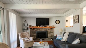 A cozy living room with a stone fireplace, a television mounted above it, and a comfortable seating area with a sofa and armchair. - Lovely 3BR/2BA Lakehouse Retreat in Gated Dubois, PA—Near Beach, Woods & Privacy (DuBois)