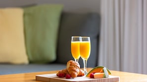 A breakfast setting with croissants, raspberries, a melon slice, and two glasses of orange juice on a wooden board.