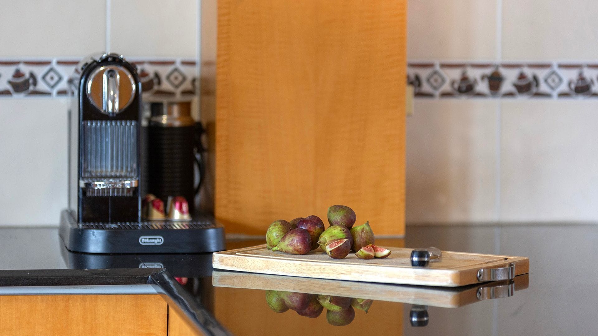 A kitchen with a coffee maker, a cutting board with fruit, and a tiled backsplash.