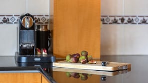 A kitchen with a coffee maker, a cutting board with fruit, and a tiled backsplash.