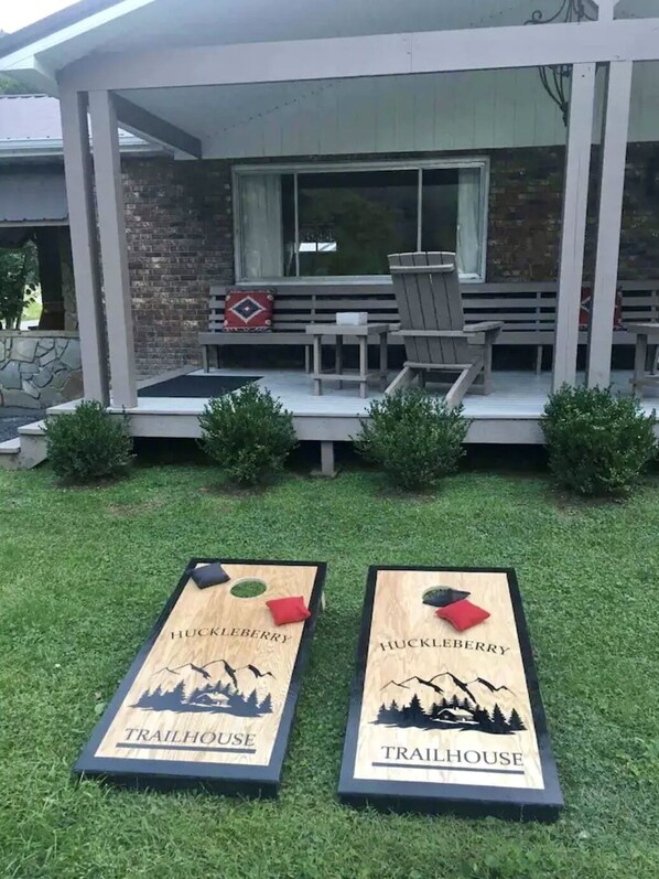 Una casa con un portico coperto, un muro in mattoni e una finestra. Due pannelli di legno sul prato riportano la scritta 'Huckleberry Trailhouse'.