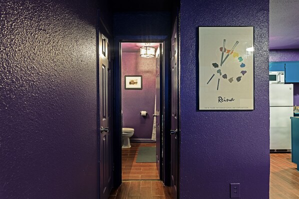 A hallway with purple walls, a framed artwork, and a visible toilet. - Amethyst Dreamscape Studio! Medical Center 01 ⭐️⭐️⭐️⭐️⭐️ (Houston)