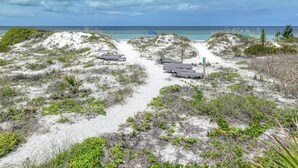Una playa con dunas de arena, un camino y sombrillas.