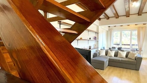 A modern interior with a wooden staircase, a grey sofa, and a kitchen area in the background. - Mountain Escape Chalet - BBQ and Mountain View (Bușteni)