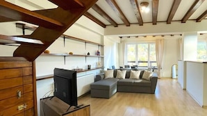 A spacious living room with a wooden staircase, a grey sectional sofa, and a TV on a wooden stand. - Mountain Escape Chalet - BBQ and Mountain View (Bușteni)