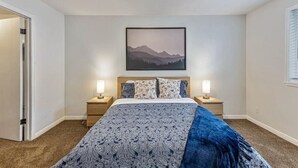 A bedroom with a bed, two bedside tables, a nightstand, a wall-mounted picture, and a door. - Sandy Ski Cottage | Central | Free Massage* | Patio (Sandy)