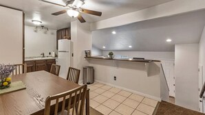 A dining area with a wooden table and chairs, a ceiling fan, recessed lighting, and a kitchen in the background. - Sandy Ski Cottage | Central | Free Massage* | Patio (Sandy)