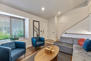 A modern living room with a sofa, armchairs, and a coffee table. There is a staircase leading to another level.