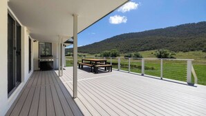 Une terrasse en bois avec un barbecue et une table de pique-nique, offrant une vue sur un paysage verdoyant et des collines.