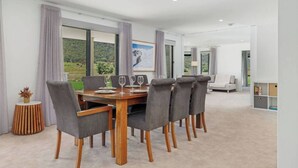 Un espace repas avec une table en bois et des chaises à revêtement gris, de grandes fenêtres offrant une vue sur la verdure et un aménagement intérieur moderne.