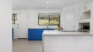 Une cuisine moderne avec des meubles blancs, un plan de travail bleu et une fenêtre donnant sur un paysage verdoyant.