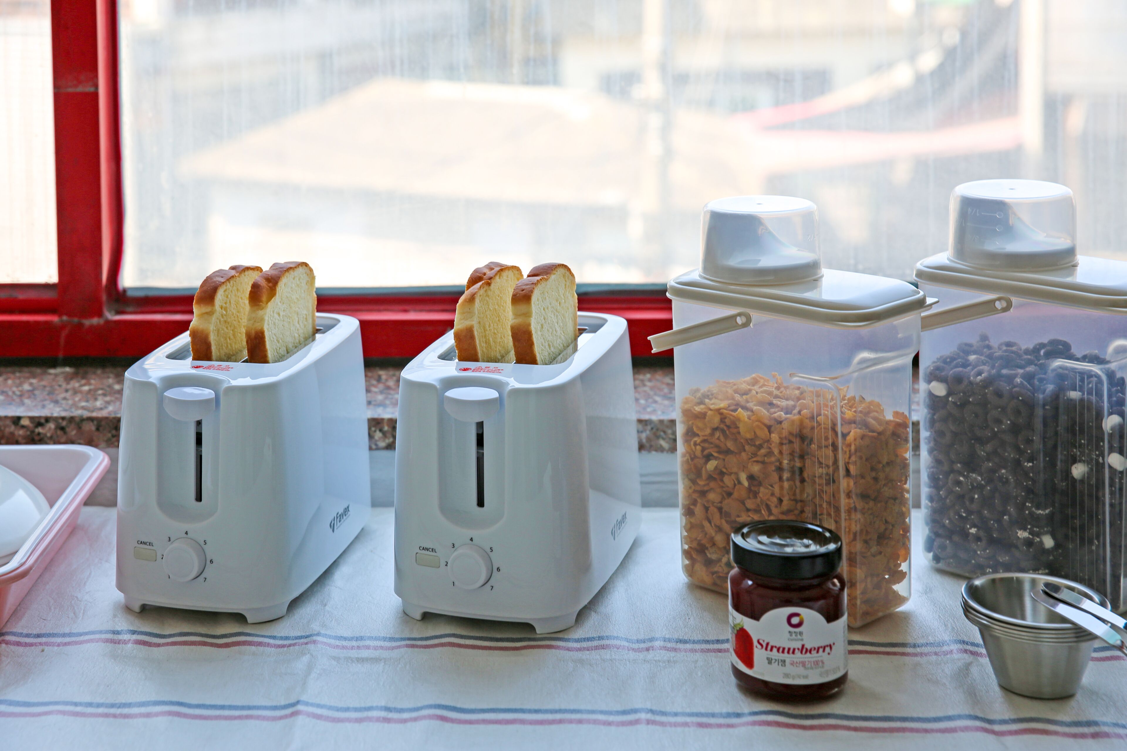 Two white toasters on a table with a jar of strawberry jam and a container of blueberries.