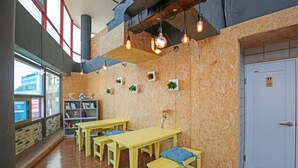 A room with wooden walls, a bookshelf, a wooden table with benches, and a door with a sign. - Dashim Guest House (Gunsan)