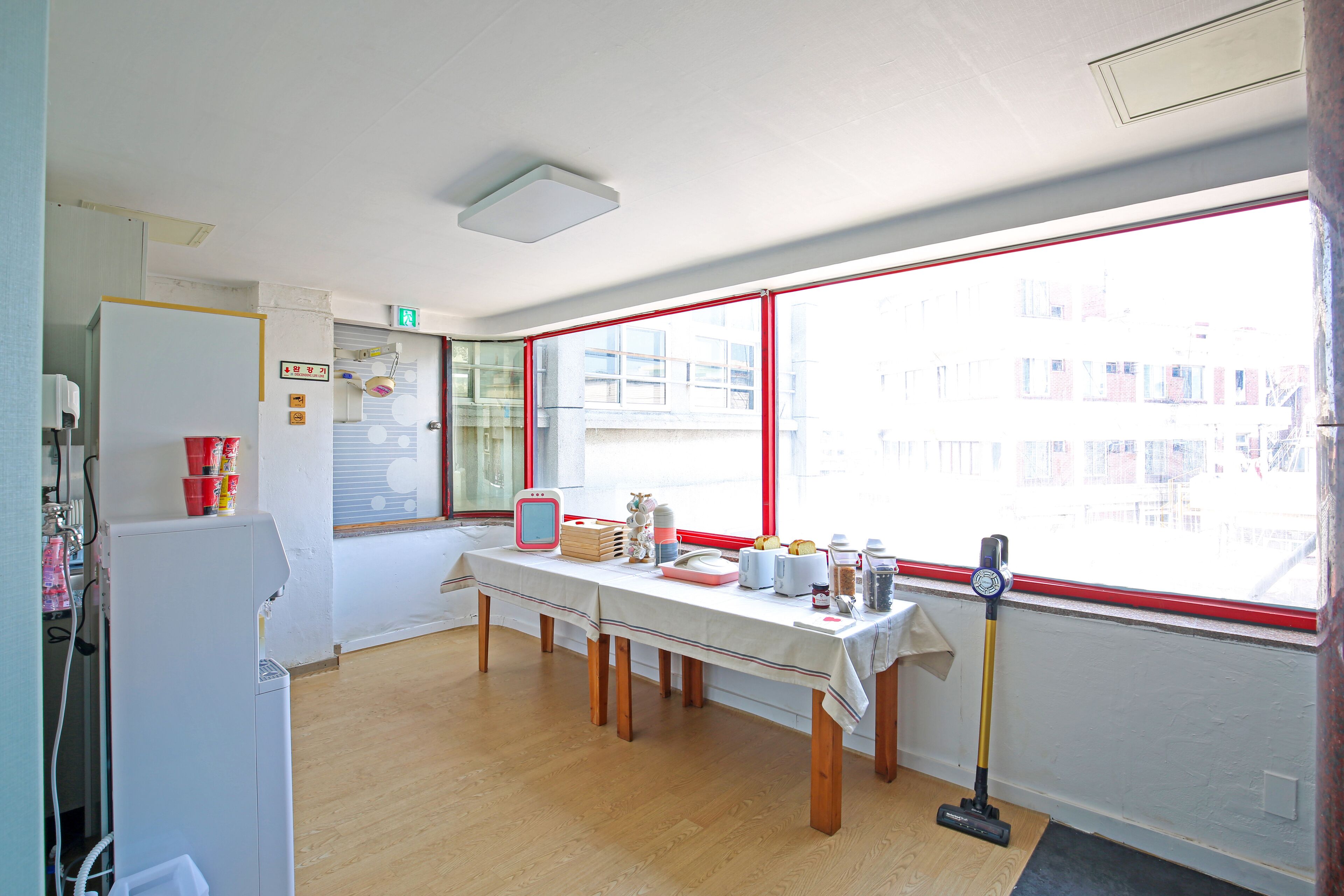 A kitchen with a table, a refrigerator, and a window with a red frame.