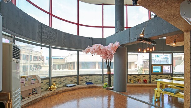 A spacious indoor area with large windows, wooden flooring, and a central column. - Dashim Guest House (Gunsan)