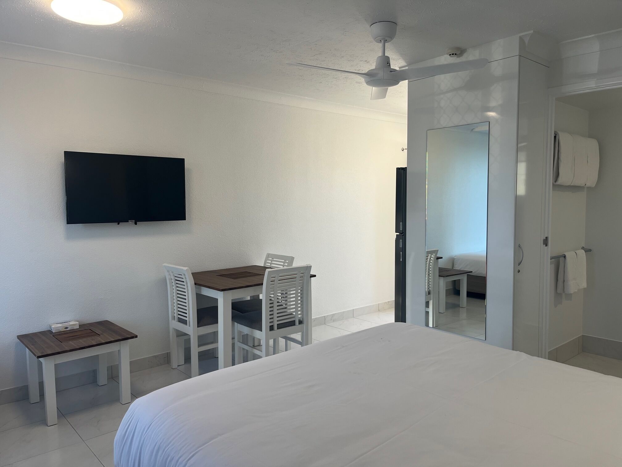 Une chambre d’hôtel comprenant un lit, un bureau avec une chaise, un téléviseur fixé au mur et un ventilateur de plafond.