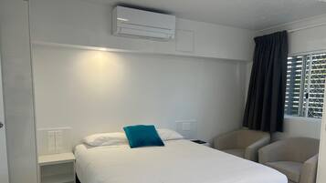 Habitación de hotel con cama, una silla, mesita de noche y equipo de aire acondicionado.