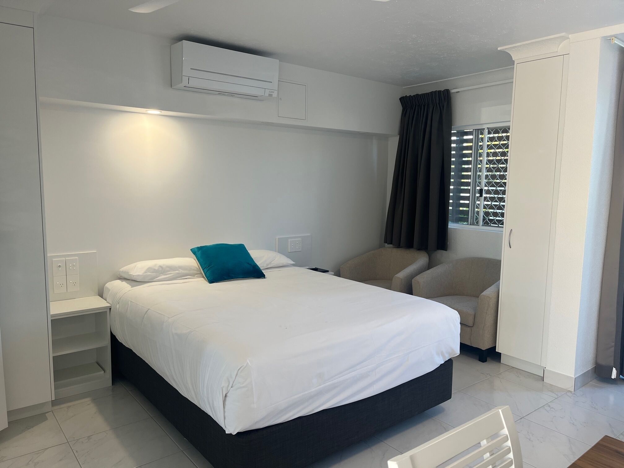 Een slaapkamer met een bed, nachtkastjes, een kledingkast, een raam met gordijnen en een airconditioning.