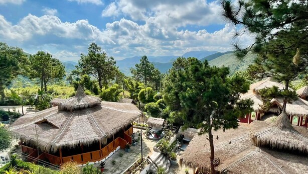 A resort with thatched-roof huts, surrounded by lush greenery and mountains in the background. - Myat Saytaman Traditional Bamboo House (Kalaw)
