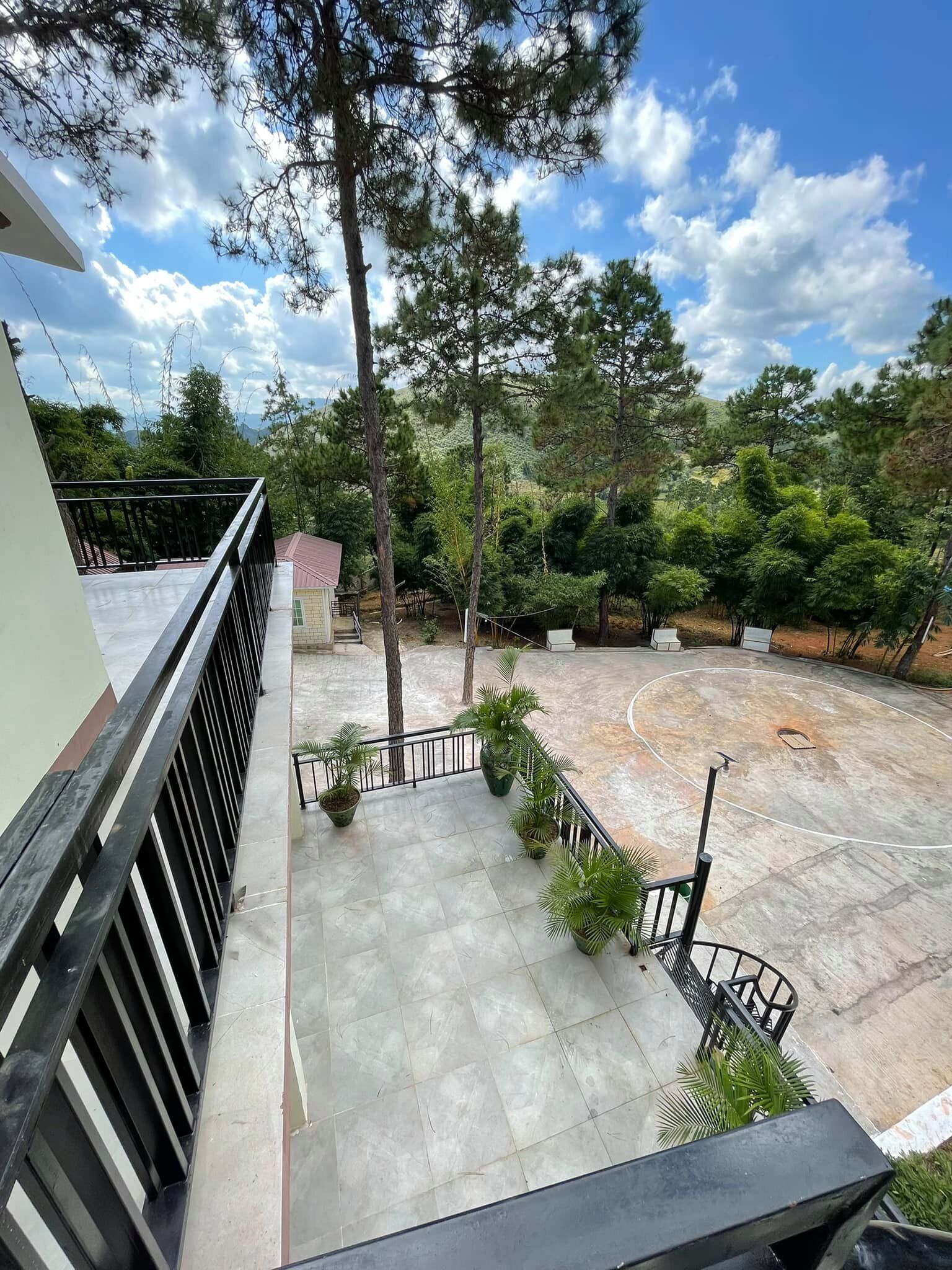 A balcony with a view of a basketball court surrounded by trees and a building.