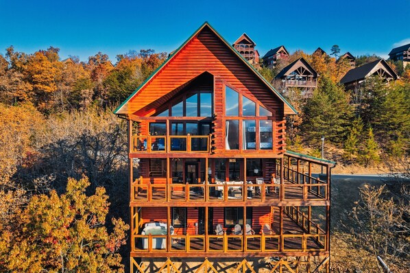 A multi-story log cabin with a balcony and large windows, surrounded by autumn foliage. - 5 Starr Views! Hot Tub Games. Sleeps 20 5 BR 4.5 baths. Close to Dollywood (Sevierville)