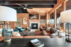 L’intérieur d’un chalet confortable, avec des murs en bois, une cheminée, des fauteuils confortables et un téléviseur fixé au-dessus de la cheminée.