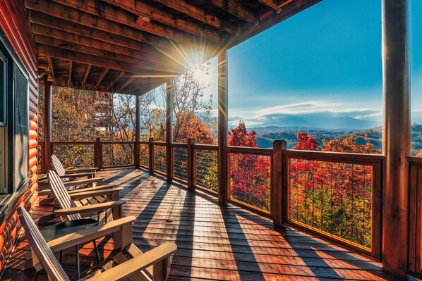 Une terrasse en bois avec des fauteuils Adirondack, une balustrade en bois et une vue sur le feuillage automnal.