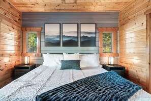 Une chambre aux murs lambrissés, avec un lit, des oreillers, une couverture et trois tableaux encadrés accrochés au mur.