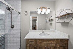 Un baño con ducha, lavamanos, armarios de madera y un espejo iluminado.