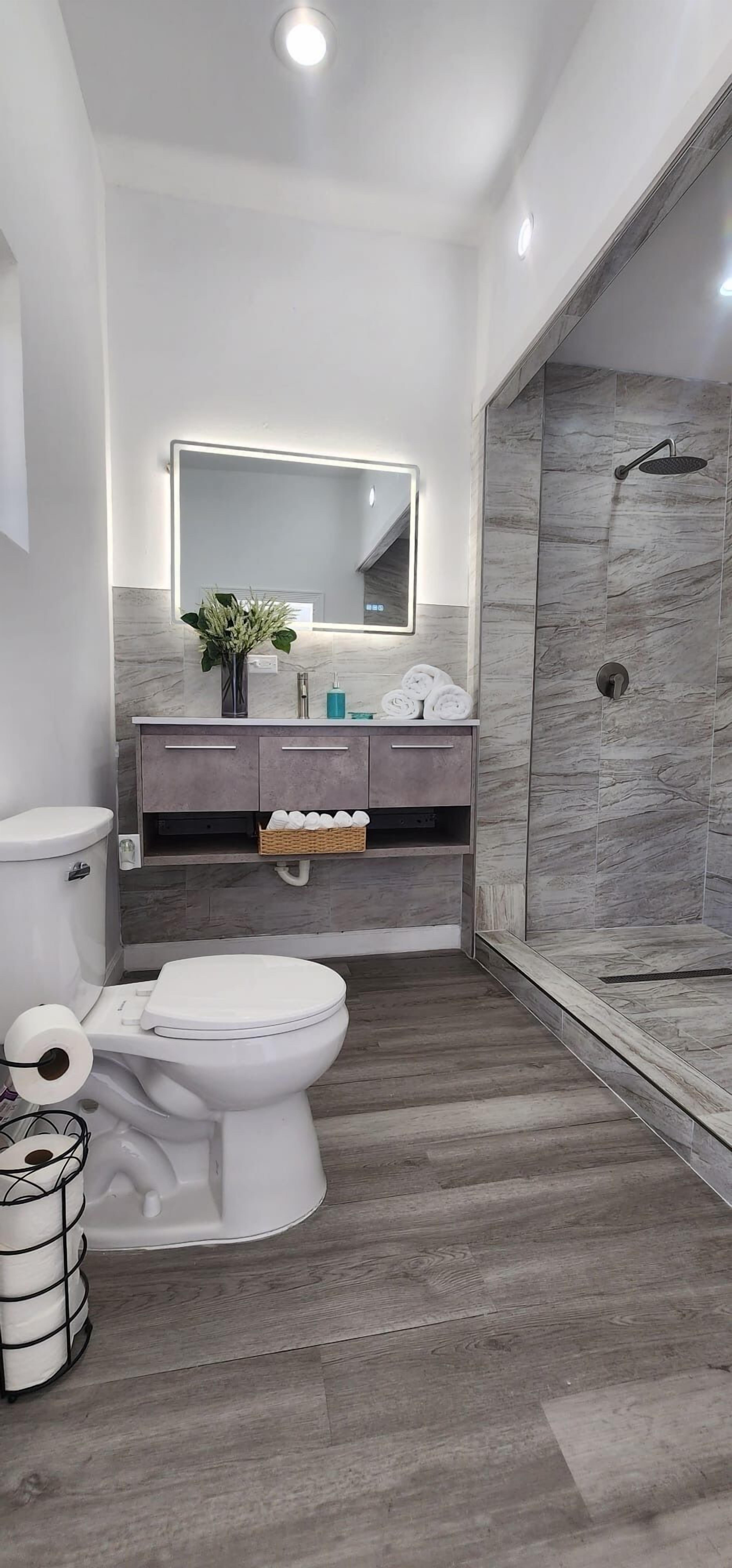 Une salle de bain moderne comprenant des toilettes, un meuble-lavabo avec un miroir, une douche et un plancher en bois.
