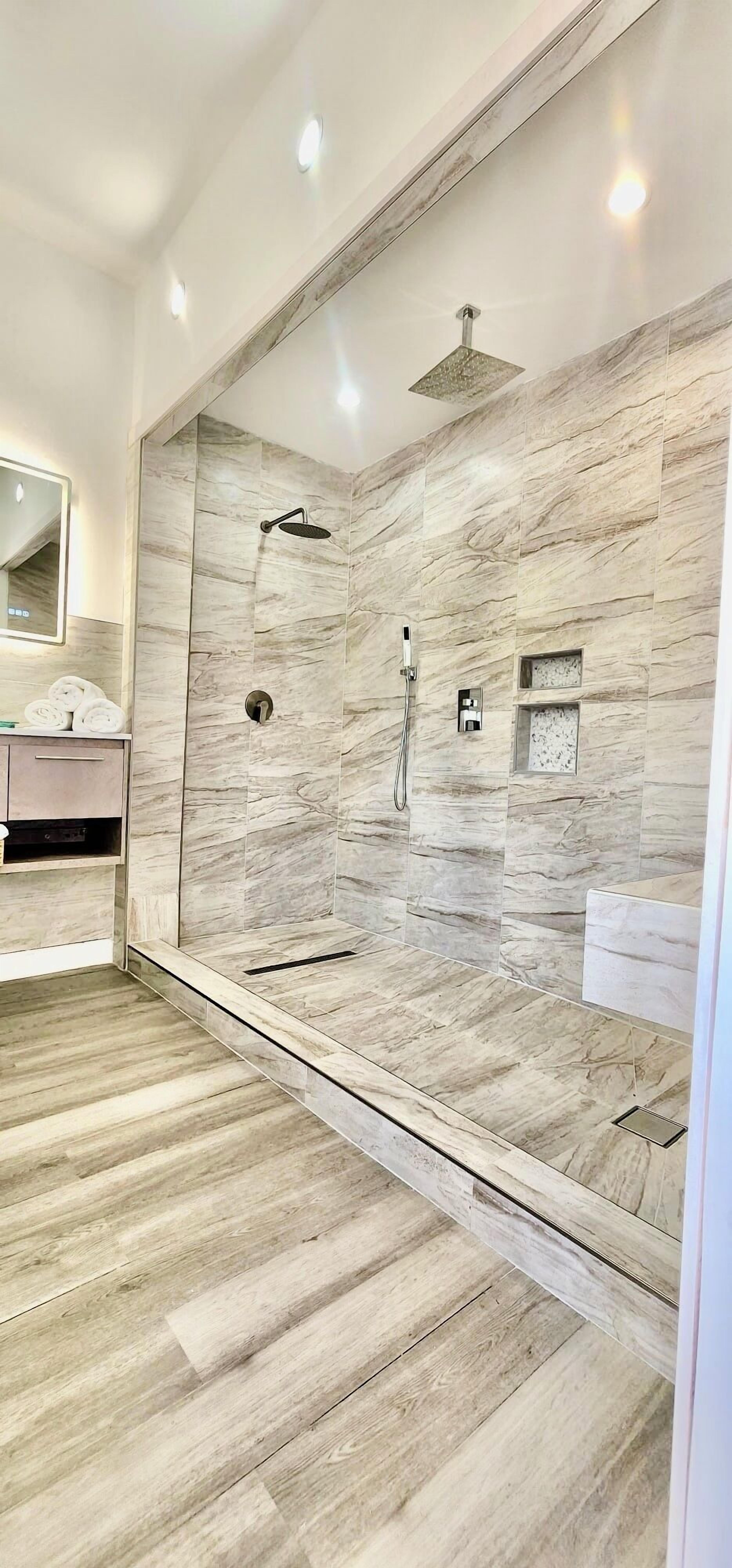 A modern bathroom with a glass-enclosed shower, marble walls, and a wooden floor.