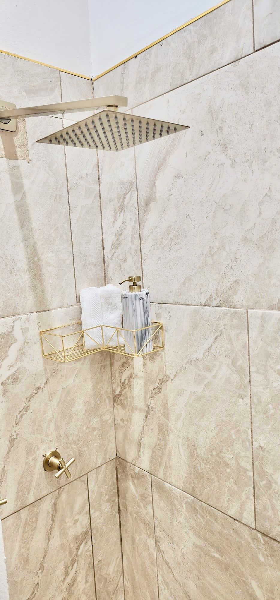 A bathroom with a shower, marble tiles, and a towel rack.
