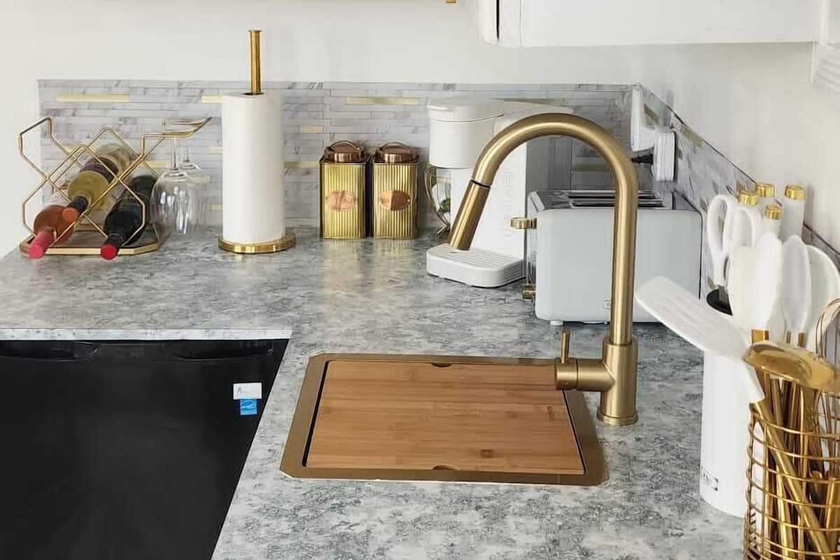 A modern kitchen with white cabinets, gold handles, a black induction cooktop, a wooden cutting board, and a stainless steel sink.