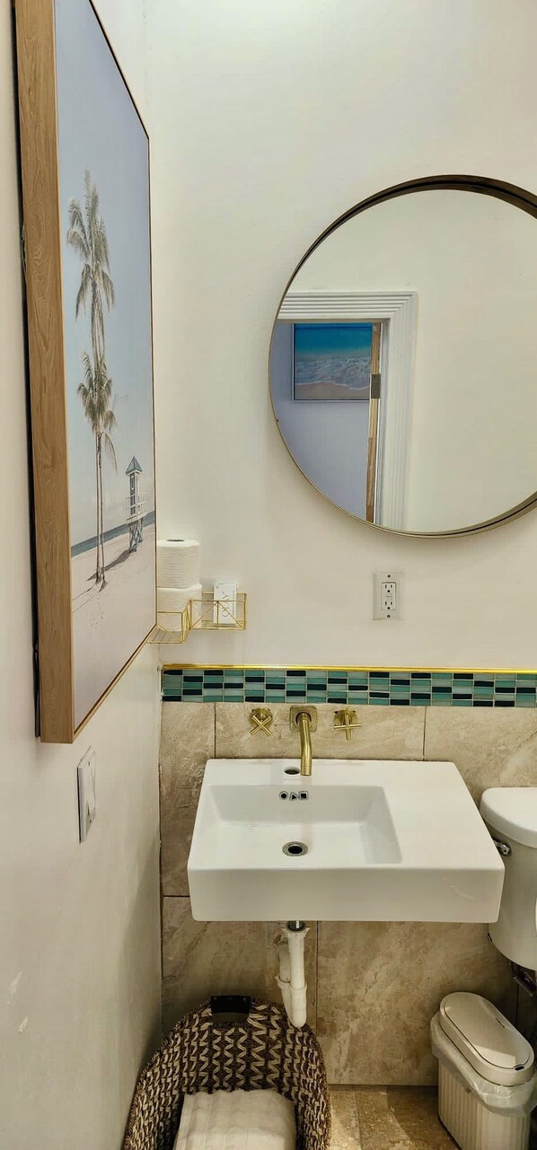 A bathroom with a white sink, a mirror, and a toilet. - The Suite Life (Rokers Point)