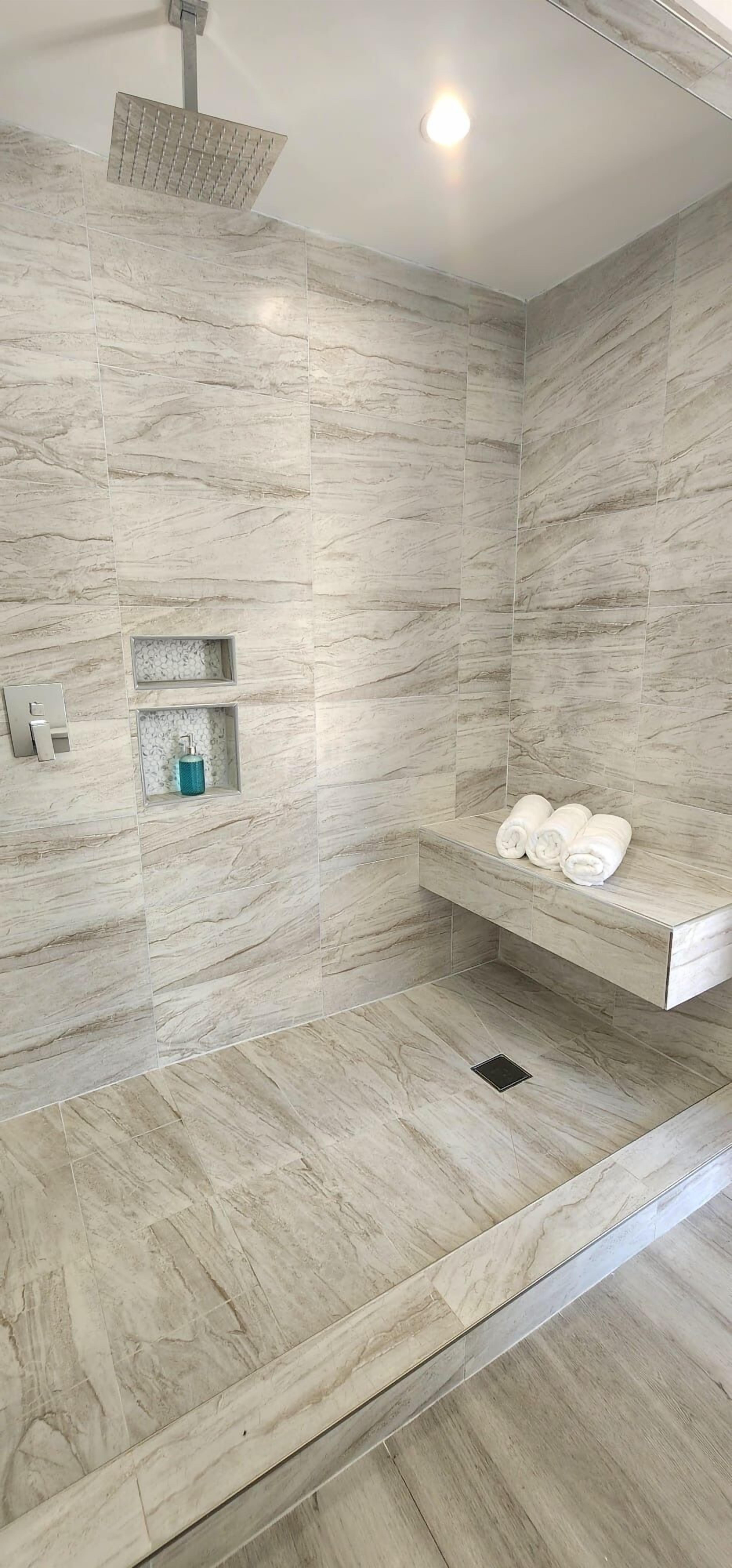 A modern shower with a built-in shelf holding towels, a handheld showerhead, and a small shelf with toiletries.